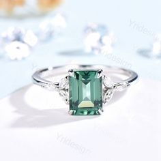 an emerald colored stone surrounded by diamonds on a white surface with other jewelry items in the background