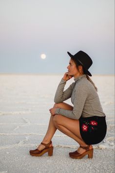 a woman sitting on the ground wearing a black hat and skirt with her legs crossed