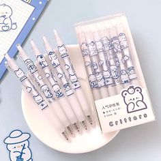 six hello kitty pens sitting on top of a white plate next to a blue notebook