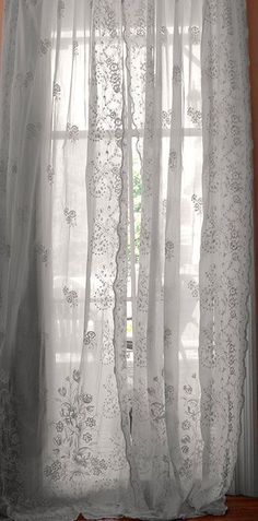 a window with sheer curtains and white lace on the curtain rod, in front of a wooden floor