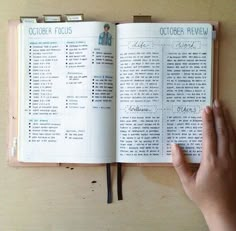 a person holding an open book on top of a wooden table