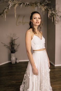 a woman in a white dress standing on a wooden floor with flowers hanging from the ceiling