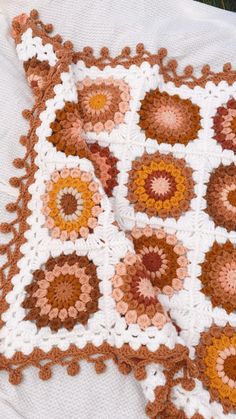 a crocheted blanket is laying on top of a white tablecloth with an orange and brown flower design