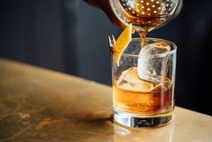 a person pouring an alcoholic drink into a glass with ice and orange peels on the rim