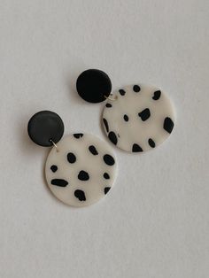 two black and white polka dot earrings on top of a white surface with one earring in the shape of a circle