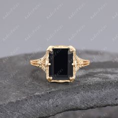 a gold ring with a black stone in the center on top of a gray rock