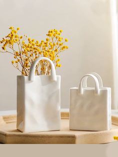 two white bags sitting next to each other on a wooden tray with yellow flowers in them