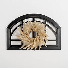 a wreath is hanging on the wall in front of a white wall with a black frame