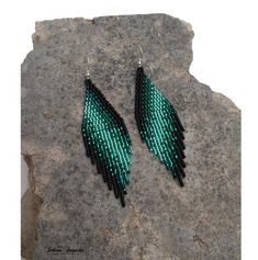 green and black beaded earrings sitting on top of a gray rock next to a stone