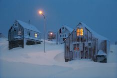 some houses are covered in snow and one is lit up by a street lamp at night