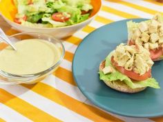 a sandwich with lettuce, tomato and chicken on it next to a bowl of dressing