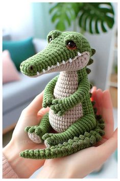 a crocheted stuffed alligator sitting on top of someone's hand in front of a couch