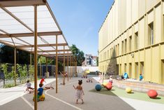 children are playing in an outdoor play area next to a building with yellow and white walls