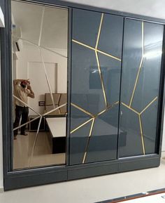 a man standing in front of a large mirror with gold lines on it's side