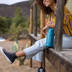 a woman sitting on a wooden bench holding a water bottle and smiling at the camera