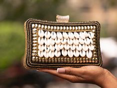 Enriched with the affirming symbol of wealth, our the Mozwi Evening Clutch is a beautiful and exclusive accessory. Crafted from cowrie shells, beads, and a detachable chain, this purse adds an enigmatic and lavish sophistication to any outfit. -measures: 8 x 5 inches -material: cowrie, beeds, threading, metal -handmade -imported Elegant White Cowrie Shell Jewelry, Handmade Bohemian Gold Clutch, Bohemian Handmade Gold Clutch, Bohemian Beaded Gold Clutch, Bohemian Gold Beaded Clutch, Elegant Embellished Beach Bag, Elegant Embellished Beach Bags, Elegant Beach Clutch, Gold Clutch With Pearl Handle