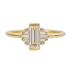 a yellow gold ring with an emerald and baguettes set in the center, on a white background