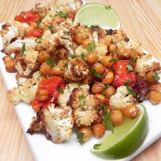 a white plate topped with cauliflower and tomatoes next to a lime wedge on top of a wooden table