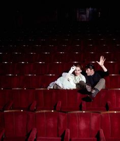 a man and woman sitting in the middle of an empty theater with their hands up