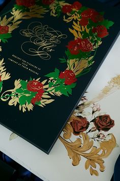 a black book with red and green flowers on it sitting on a table next to other items