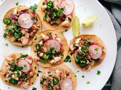 four tacos on a white plate topped with meat and veggies, garnished with cilantro