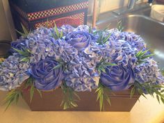 blue flowers are in a wooden box on the counter