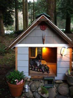 a dog is sitting in the window of a small house made out of rocks and wood