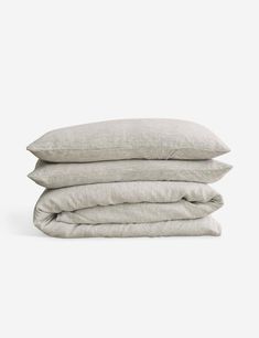 three linen pillows stacked on top of each other, one white and the other light gray