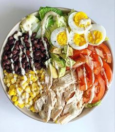 a salad with eggs, tomatoes, black beans, corn, lettuce and dressing