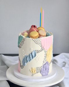 a decorated birthday cake on a plate with candles and macaroons in the middle