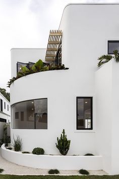 a white house with plants growing on the roof and side windows in front of it