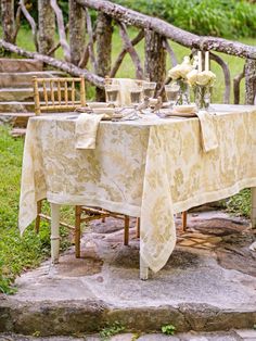 a table set up with flowers and candles on it for an outdoor dinner party in the woods