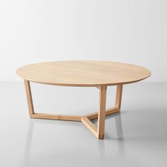 an oval table with wooden legs on a white surface, in front of a plain wall