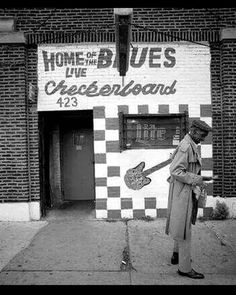 a black and white photo of a man standing in front of a building with a sign that says home of the blues