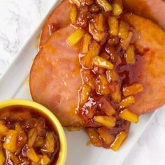 two hot dogs covered in bbq sauce on a white plate next to a yellow bowl