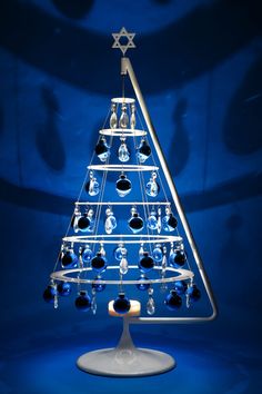 a glass christmas tree with blue lights on it's sides and ornaments hanging from the top