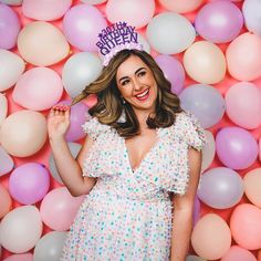 a woman standing in front of balloons with a happy birthday hat on her head and smiling at the camera