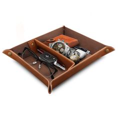 a brown leather tray with watches and other items in it on a white surface,