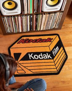 a woman sitting on the floor in front of a kodak sign and stereo speakers