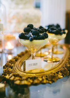 three desserts are sitting on a table with gold trimming and blueberries in them