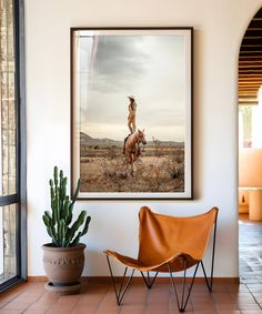 a framed photograph hangs on the wall above a chair and cactus in a living room