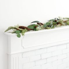 a mantel with greenery and pine cones on it in front of a white brick fireplace