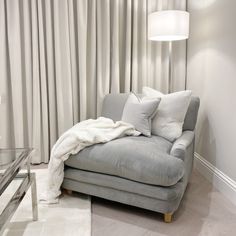 a grey couch with pillows on it in front of a white curtained wall and floor