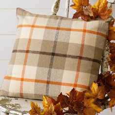 an orange plaid pillow sitting on top of a white chair next to a pile of leaves