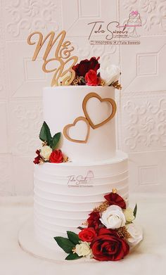 a white wedding cake with red and white flowers on the bottom tier is decorated with gold monograms