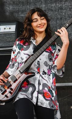 a woman holding a bass in her right hand while standing next to a guitar on stage