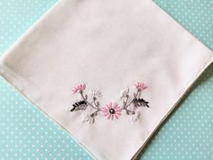 two embroidered flowers sit on top of a white napkin with blue polka dot paper in the background