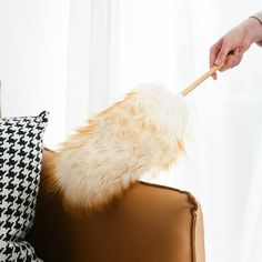 a person holding a wooden stick over a brown leather chair with black and white pillows