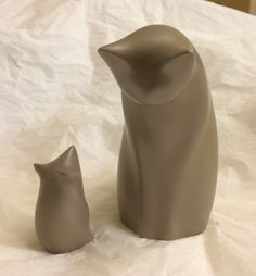 two gray ceramic figurines sitting next to each other on a white sheeted surface