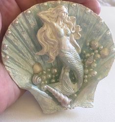 there is a small shell with a mermaid on it and pearls in the shells around it